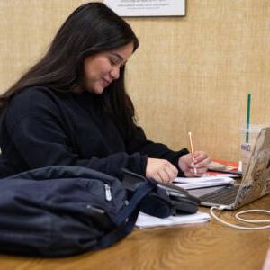 Female student studying in the library with her laptop and notes.